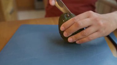 Kadın mutfak tahtasındaki taze avokadoyu dilimlere ayırıyor. Ellerinizi yakınlaştırın ve sağlıklı yemekleri pişirmek için olgun avokado ve salata ile hazırlayın..