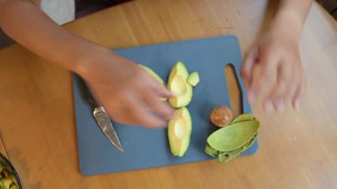 Kadın mutfak tahtasındaki taze avokadoyu dilimlere ayırıyor. Ellerinizi yakınlaştırın ve sağlıklı yemekleri pişirmek için olgun avokado ve salata ile hazırlayın..