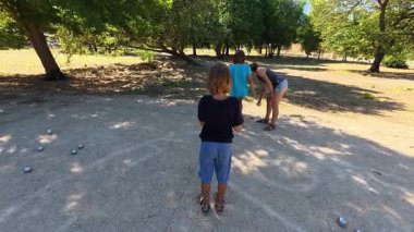 Aile parkta birlikte petanque oynuyor. Yetişkinler ve çocuklar güneşli bir yaz gününde sırayla metal toplar atıyorlar. Eğlenceli bir açık hava aktivitesi ve aile bağları oyunu.