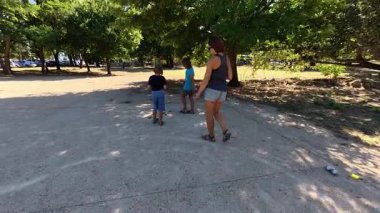Aile parkta birlikte petanque oynuyor. Yetişkinler ve çocuklar güneşli bir yaz gününde sırayla metal toplar atıyorlar. Eğlenceli bir açık hava aktivitesi ve aile bağları oyunu.