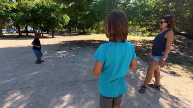 Aile parkta birlikte petanque oynuyor. Yetişkinler ve çocuklar güneşli bir yaz gününde sırayla metal toplar atıyorlar. Eğlenceli bir açık hava aktivitesi ve aile bağları oyunu.