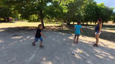 Aile parkta birlikte petanque oynuyor. Yetişkinler ve çocuklar güneşli bir yaz gününde sırayla metal toplar atıyorlar. Eğlenceli bir açık hava aktivitesi ve aile bağları oyunu.