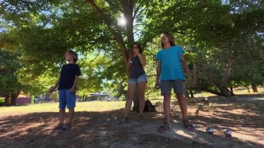 Aile parkta birlikte petanque oynuyor. Yetişkinler ve çocuklar güneşli bir yaz gününde sırayla metal toplar atıyorlar. Eğlenceli bir açık hava aktivitesi ve aile bağları oyunu.