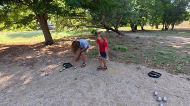 Güneşli bir günde iki çocuk açık havada Petanque oynuyor. Çocuklar sırayla parktaki çakıl taşlarına metal toplar atıyor, eğlence ve spor aktivitelerinin keyfini çıkarıyorlar..
