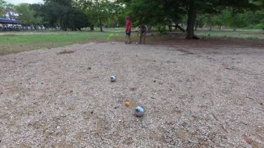 Güneşli bir günde iki çocuk açık havada Petanque oynuyor. Çocuklar sırayla parktaki çakıl taşlarına metal toplar atıyor, eğlence ve spor aktivitelerinin keyfini çıkarıyorlar..