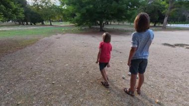 Güneşli bir günde iki çocuk açık havada Petanque oynuyor. Çocuklar sırayla parktaki çakıl taşlarına metal toplar atıyor, eğlence ve spor aktivitelerinin keyfini çıkarıyorlar..