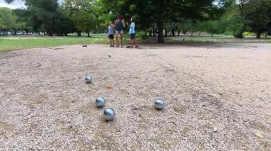 Aile parkta birlikte petanque oynuyor. Yetişkinler ve çocuklar güneşli bir yaz gününde sırayla metal toplar atıyorlar. Eğlenceli bir açık hava aktivitesi ve aile bağları oyunu.