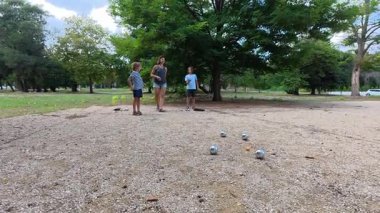 Aile parkta birlikte petanque oynuyor. Yetişkinler ve çocuklar güneşli bir yaz gününde sırayla metal toplar atıyorlar. Eğlenceli bir açık hava aktivitesi ve aile bağları oyunu.