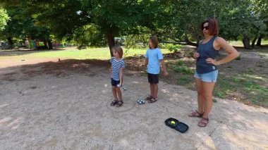 Aile parkta birlikte petanque oynuyor. Yetişkinler ve çocuklar güneşli bir yaz gününde sırayla metal toplar atıyorlar. Eğlenceli bir açık hava aktivitesi ve aile bağları oyunu.