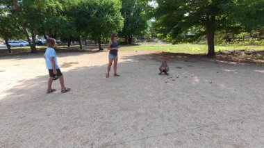 Aile parkta birlikte petanque oynuyor. Yetişkinler ve çocuklar güneşli bir yaz gününde sırayla metal toplar atıyorlar. Eğlenceli bir açık hava aktivitesi ve aile bağları oyunu.