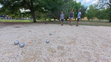 Aile parkta birlikte petanque oynuyor. Yetişkinler ve çocuklar güneşli bir yaz gününde sırayla metal toplar atıyorlar. Eğlenceli bir açık hava aktivitesi ve aile bağları oyunu.