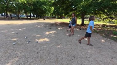 Aile parkta birlikte petanque oynuyor. Yetişkinler ve çocuklar güneşli bir yaz gününde sırayla metal toplar atıyorlar. Eğlenceli bir açık hava aktivitesi ve aile bağları oyunu.