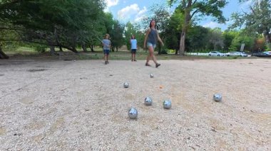 Aile parkta birlikte petanque oynuyor. Yetişkinler ve çocuklar güneşli bir yaz gününde sırayla metal toplar atıyorlar. Eğlenceli bir açık hava aktivitesi ve aile bağları oyunu.