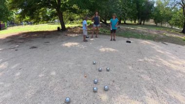 Aile parkta birlikte petanque oynuyor. Yetişkinler ve çocuklar güneşli bir yaz gününde sırayla metal toplar atıyorlar. Eğlenceli bir açık hava aktivitesi ve aile bağları oyunu.