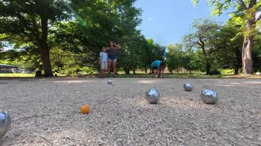 Aile parkta birlikte petanque oynuyor. Yetişkinler ve çocuklar güneşli bir yaz gününde sırayla metal toplar atıyorlar. Eğlenceli bir açık hava aktivitesi ve aile bağları oyunu.