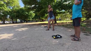 Aile parkta birlikte petanque oynuyor. Yetişkinler ve çocuklar güneşli bir yaz gününde sırayla metal toplar atıyorlar. Eğlenceli bir açık hava aktivitesi ve aile bağları oyunu.