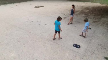 Aile parkta birlikte petanque oynuyor. Yetişkinler ve çocuklar güneşli bir yaz gününde sırayla metal toplar atıyorlar. Eğlenceli bir açık hava aktivitesi ve aile bağları oyunu.