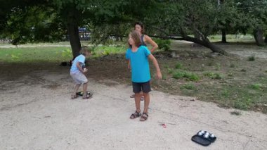 Aile parkta birlikte petanque oynuyor. Yetişkinler ve çocuklar güneşli bir yaz gününde sırayla metal toplar atıyorlar. Eğlenceli bir açık hava aktivitesi ve aile bağları oyunu.