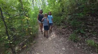 Orman yolunda yürüyen bir aile. Kadın ve iki çocuk yaz yürüyüşünün tadını çıkarıyor. Bir çocuk doğayı, boş zamanları, açık hava aktivitelerini ve birlikte vakit geçirmeyi keşfederken sabun köpükleri üflüyor..