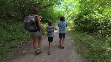 Aile bir orman patikası boyunca birlikte yürüyor. Sırt çantalı bir kadın ve iki çocuk doğayı keşfediyor. Yürüyüş, açık hava macerası, yaz tatili ve ormanda kaliteli zaman geçirme..