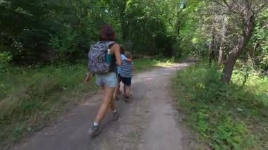 Aile bir orman patikası boyunca birlikte yürüyor. Sırt çantalı bir kadın ve iki çocuk doğayı keşfediyor. Yürüyüş, açık hava macerası, yaz tatili ve ormanda kaliteli zaman geçirme..