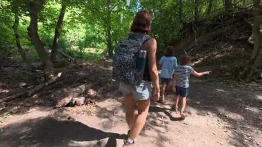 Aile bir orman patikası boyunca birlikte yürüyor. Sırt çantalı bir kadın ve iki çocuk doğayı keşfediyor. Yürüyüş, açık hava macerası, yaz tatili ve ormanda kaliteli zaman geçirme..