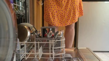 Kadın bulaşık makinesini evde boşaltıyor, bulaşıkları ve çatal bıçakları kaldırıyor. Günlük ev işleri, mutfak rutini ve modern yaşam tarzı..