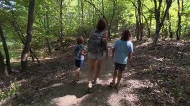 Aile bir orman patikası boyunca birlikte yürüyor. Sırt çantalı bir kadın ve iki çocuk doğayı keşfediyor. Yürüyüş, açık hava macerası, yaz tatili ve ormanda kaliteli zaman geçirme..