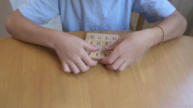 Masada numaralandırılmış fayanslarla ahşap sürgülü bulmacayı çözen çocuğun yakın çekimi. Beyin eğitimi, problem çözme, mantık oyunları, çocukluk eğitimi ve bilişsel gelişim kavramı.