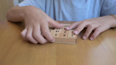 Masada numaralandırılmış fayanslarla ahşap sürgülü bulmacayı çözen çocuğun yakın çekimi. Beyin eğitimi, problem çözme, mantık oyunları, çocukluk eğitimi ve bilişsel gelişim kavramı.