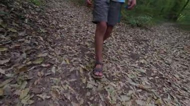 Çocuğun ormanda şort ve sandalet giyerek yürüdüğü yakın plan. Açık hava macerası, doğa yürüyüşü ve keşfi..