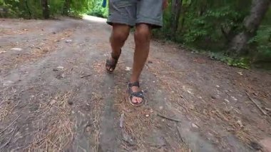 Çocuğun ormanda şort ve sandalet giyerek yürüdüğü yakın plan. Açık hava macerası, doğa yürüyüşü ve keşfi..