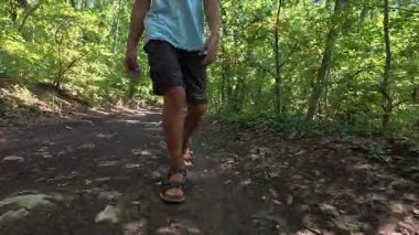 Çocuğun ormanda şort ve sandalet giyerek yürüdüğü yakın plan. Açık hava macerası, doğa yürüyüşü ve keşfi..