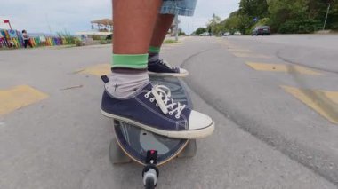 Close-up of feet in sneakers riding a surfskate on a seaside promenade, low angle view with ocean and stormy sky in background.