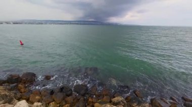 Dark storm clouds forming over the sea with city coastline in the background, dramatic weather as rain begins to fall.