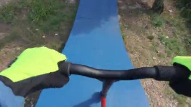 POV shot of riding a red scooter on a blue pump track, hands on handlebars in gloves, active outdoor lifestyle in summer.