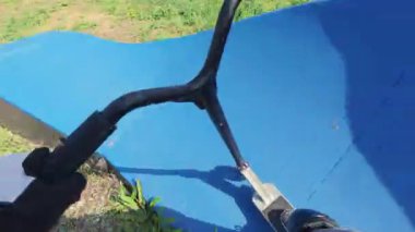 POV shot of riding a red scooter on a blue pump track, hands on handlebars in gloves, active outdoor lifestyle in summer.