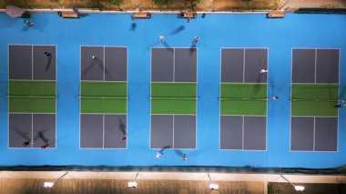 Aerial view of multiple pickleball courts with players in action, top down perspective of sport game, people playing recreational match under lights.
