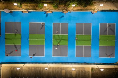 Aerial view of multiple pickleball courts with players in action, top down perspective of sport game, people playing recreational match under lights.