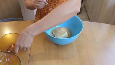 Mixing dough with egg in a blue bowl, close up of cooking process on wooden table, homemade baking preparation in kitchen.