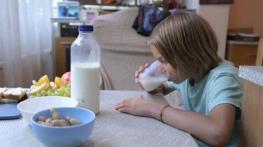 Young boy drinking milk from a glass at a kitchen table with fresh fruit and avocado slices, enjoying a healthy snack at home.