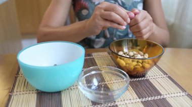 Hands shelling pistachios into bowls on a kitchen table, preparing a healthy snack at home.