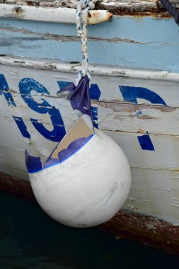 Old boat fenders and nautical ropes on rusty ship. Weathered buoys on old vessel with pilled paint. Old fishing boat