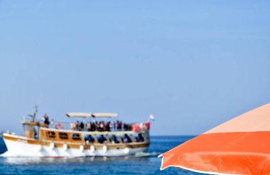 Parasol an ship full of tourists in background. Tourist boat, blur background