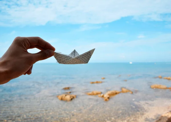 Hand holding paper boat, sea background. Travel and adventure concept. Paper boat in hand