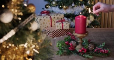 Kız kırmızı bir Noel mumu yakıyor. Kırmızı, beyaz, yeşil ve altın rengi arkaplanda Noel çelengi ve hediyeler. Yüksek kalite 4k görüntü