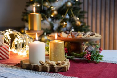 Tahtanın üzerinde yanan beyaz ve altın rengi üç mum Noel masasının kırmızı ve beyaz masa örtüsü üzerinde duruyor. Yüksek kalite fotoğraf