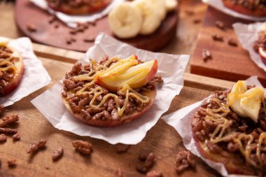 Tatil için yaratıcı parti atıştırmalığı. Fıstık ezmeli elma turları, karamelli ve çikolatalı. Muz dilimli pirinç kabartması. Çocuklar ve yetişkinler için ilginç bir aperatif..