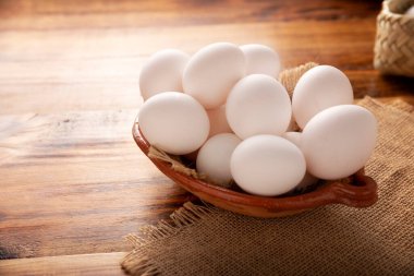 A dozen white chicken eggs in a clay container on a rustic wooden table. Very popular nutritious and economic food product. Close-up image.