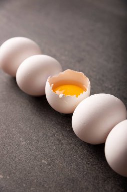 White chicken eggs and egg yolk in a row on black stone table. Very popular nutritious and economic food product. Concept image. Closeup view.